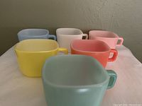 Front view of six square Glasbake mugs in pastel colors arranged in two rows showing colors and shape.