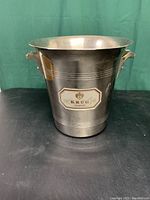 Front view of Krug silver-color metal ice bucket showing handles and logo on front.