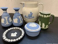 Photo showing six pieces of vintage Wedgwood including blue vases, blue lidded dish, black pin dish, green and white pitchers with classical scenes in white and blue relief