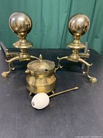 Front and side view of brass andirons, smudge pot, and wand with pumice stone all displayed on black surface.