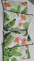 Four rectangular decorative pillows with tropical leaf and flower pattern, laid out on a white surface, showing front design and piping detail.