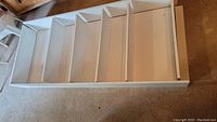 Unassembled white Ikea Billy bookcase frame and shelves laid on floor showing five shelf slots and side panels