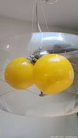 Side view showing three bright yellow globe shades clustered around the central chrome fixture with a large clear outer glass shade suspended around them.