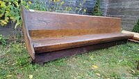 Front profile view of the wooden church pew on grass.