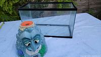 Photo showing both the clear rectangular fish tank and the Super Soaker toy shaped like a blue stone face with foliage.
