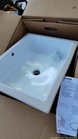White rectangular Kohler ceramic sink in open cardboard box, showing drain and overflow holes.