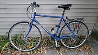 Side profile of blue Peugeot bicycle showing frame, wheels, saddle, rack and pedals