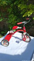 Side view of the red and chrome retro Radio Flyer tricycle showing the seat, rear wheels, and handlebar grips.