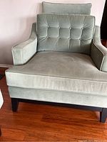 Front view of light green upholstered armchair showing cushioned seat, armrests, and button-tufted backrest.