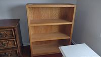 Front view of solid wood bookcase with three shelves against a wall.