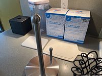 Photo showing two boxed large glass storage jars with bamboo lids, a clear plastic container, and a stainless steel paper towel holder on countertop