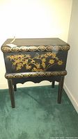 Full view of small black chest on legs, showing hand-painted gold bird and floral motifs with decorative borders.