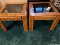 Pair of two oak end tables with glass insert tops, showing the wood grain and glass surface from an angled top view.