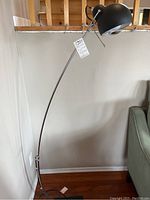 Full view of the black adjustable floor lamp standing against wall, showing curved metal arm and square base.