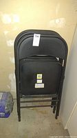 Three stacked black metal folding chairs with padded vinyl seats and backrests.