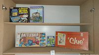 Cabinet shelf with 4 boxed games: The Electronic Learning Machine, Waterworks, Battleship, and Clue.