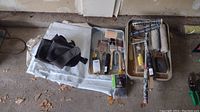 Photo showing paint brushes, rollers, trays and a folded tarp sheet on the ground