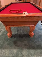 Front view of oak wood pool table base, carved claw feet, red felt visible