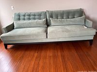 Full front view of light green tufted sofa showing two cushions, wooden legs and curved arms.