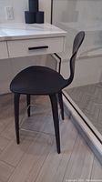 Black counter height stool facing sideways showing seat, leg structure and footrest.
