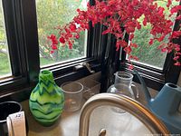 Photo of five vases and glassware on kitchen window ledge near sink.