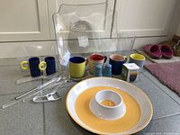 Wide view of the lot with coffee mugs, espresso cups, salt and pepper shakers, clear salad bowl, chip and dip platter and silicone muffin cups arranged on floor