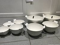 Six white porcelain bowls arranged by size on tiled floor, two largest in back