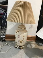 Photo of the large ceramic table lamp showing the gold floral and butterfly decoration with beige pleated lampshade