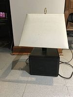 Side view of entire table lamp showing dark brown leather base and square off-white fabric shade with power cord.