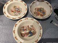 Three Royal Doulton Bunnykins porcelain baby dishes seen from above showing different Bunnykins scenes in the center and bunny motif border.