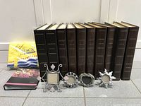 Photo of 10 large brown photo albums from Black's, 4 small decorative picture frames, and one smaller photo album with flower cover.