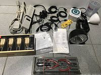 Overview of lot including hand tool set, timer, power bar, vintage Edison bulbs, adapters, headphones, spotlight, and cables.