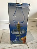 Original boxed packaging showing clear glass hurricane oil lamp with brass burner and chimney.