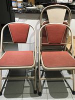 Four vintage metal folding chairs with red padded seats and backs, shown both open and folded positions indoors on tile floor near kitchen.