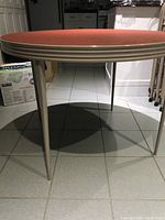 Side view of the round table showing metal legs and red fabric top