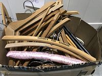 Photo showing approximately 50 wooden hangers in a box, including Eaton's Fur Storage branded hanger and pink padded hanger.