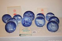 Set of all 18 Bing & Grondahl Christmas plates displayed, with original boxes and a Bing & Grondahl catalog booklet in front.