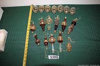 All 18 glass ornaments laid out in four rows on green cloth with measuring tape for scale, showing variety of shapes and sizes including teardrops and finials.
