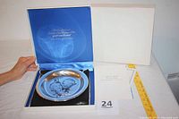 Photo showing the sterling silver collectors plate inside its original blue lined display box with lid open and paperwork beside it.