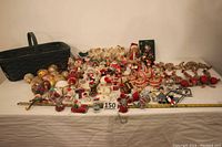 Wide shot showing entire basket and array of assorted Christmas ornaments including Santas, mice, and bells spread out on white cloth.