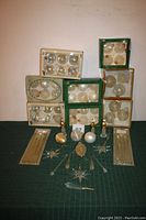 Eight boxes of clear, white, frosted, and gold glass Christmas ornaments stacked with loose ornaments arranged in front.