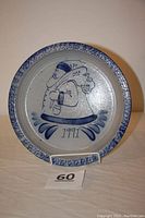 Front view of round decorative stoneware plate with blue salt glaze and painted Santa Claus image holding sack, dated 1991.