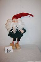 Full body front view of the elf figurine showing the red hat, white hair and beard, green coat, striped red and white socks, and wooden clogs.