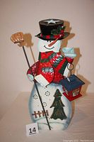 Full view of metal snowman candle holder showing painted details, scarf, hat, lantern, broom, and cut-out shapes on body.