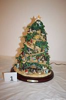 Front view of the nativity tree showing the spiral design, figurines, illuminated star on top, and base plaque