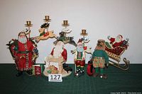 Group of six Santa collectibles including Clothique Santa, flying Santa with reindeer sleigh, golfing Santa with caddy dog, and others on a green table.