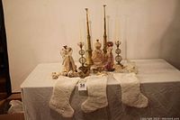 Photo showing the crochet stockings in front, Victorian dress form, angel figurines, candle sticks, and other decorations arranged on a table against a plain background.