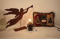 Wide shot showing metal angel sculpture, house-shaped night light with bulb lit, and Christmas themed pillow with trees and snowman pattern.