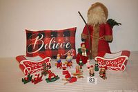 Full lot including Believe pillow, primitive Santa figure, two ceramic sleigh planters, and multiple Christmas ornaments arranged in front