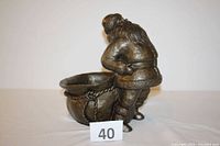 Full view of bronze tone Santa figurine leaning back on an open bag, showing details of Santa's coat, belt, and bag.